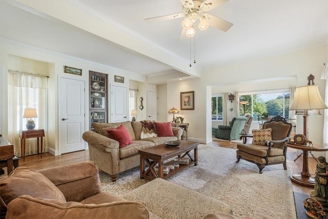 living room with crown molding, a ceiling fan, baseboards, and light wood finished floors