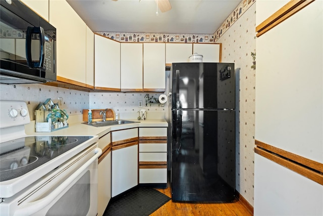 kitchen featuring light countertops, a sink, wood finished floors, black appliances, and wallpapered walls