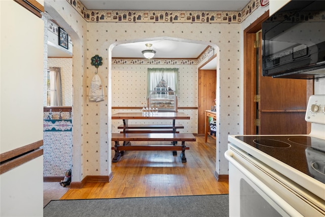 kitchen with wallpapered walls, white electric stove, arched walkways, wood finished floors, and black microwave