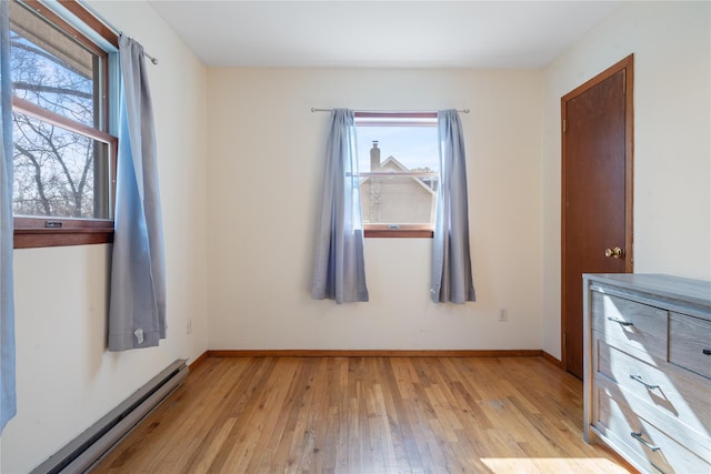 unfurnished bedroom featuring a baseboard heating unit, light wood-type flooring, multiple windows, and baseboards