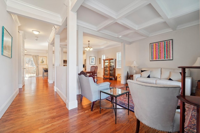 living room featuring ornamental molding, beam ceiling, light wood-style flooring, a notable chandelier, and coffered ceiling