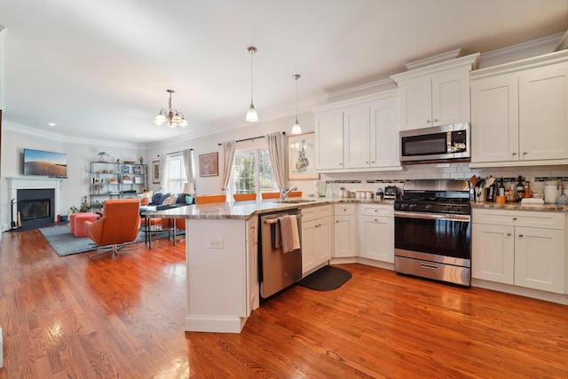 kitchen with backsplash, light wood-style flooring, appliances with stainless steel finishes, a fireplace, and a peninsula