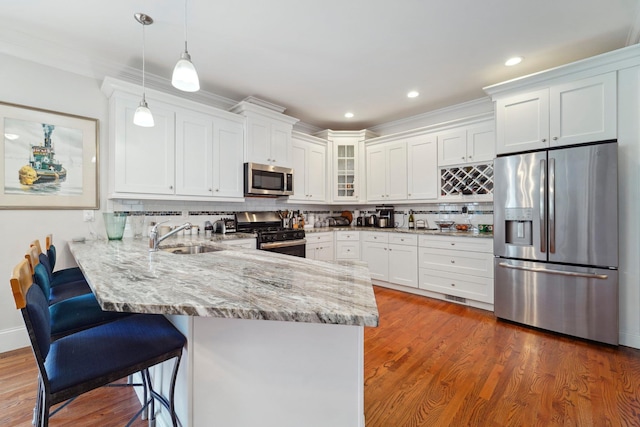 kitchen with glass insert cabinets, a peninsula, stainless steel appliances, white cabinetry, and a sink