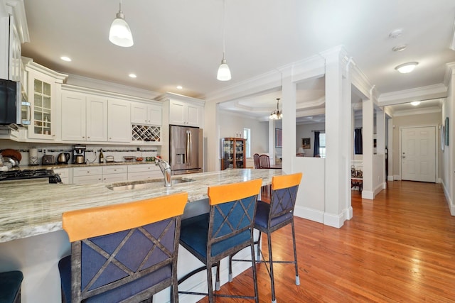 kitchen with a sink, light stone counters, a breakfast bar area, and stainless steel fridge with ice dispenser