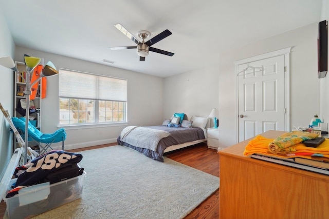 bedroom featuring ceiling fan, visible vents, baseboards, and wood finished floors