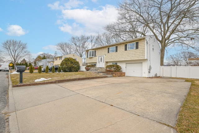 raised ranch featuring concrete driveway, an attached garage, and fence