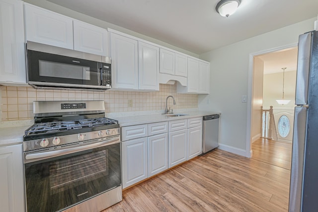 kitchen with stainless steel appliances, light countertops, white cabinets, a sink, and light wood-type flooring