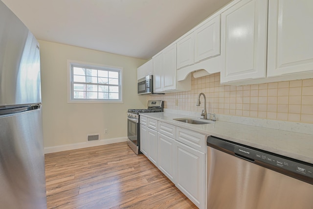 kitchen with stainless steel appliances, a sink, visible vents, light wood-style floors, and tasteful backsplash