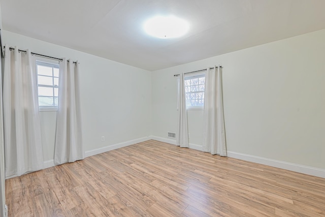 empty room with baseboards, visible vents, and light wood finished floors