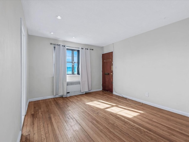 spare room featuring radiator, light wood-style flooring, and baseboards