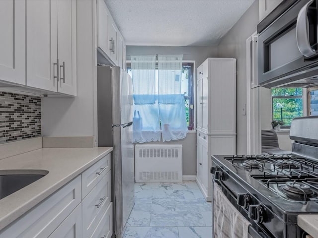 kitchen featuring radiator, marble finish floor, light countertops, black gas stove, and white cabinetry