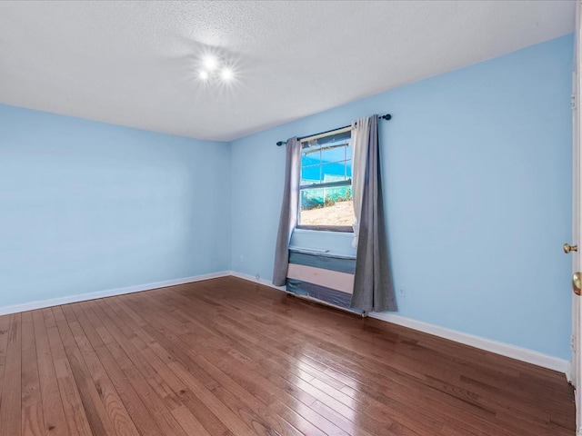 spare room featuring wood-type flooring, baseboards, and a textured ceiling