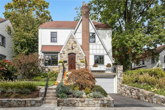 english style home with a chimney, stucco siding, an attached garage, stone siding, and driveway