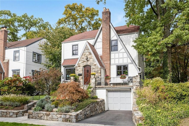 tudor-style house with driveway, a chimney, an attached garage, and stucco siding