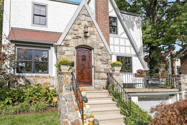 english style home with stone siding, a chimney, and stucco siding