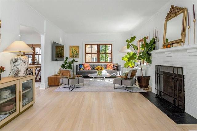 living area featuring a brick fireplace, ornamental molding, and wood finished floors