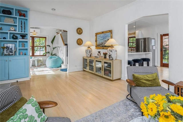 living area with arched walkways, crown molding, baseboards, and wood finished floors