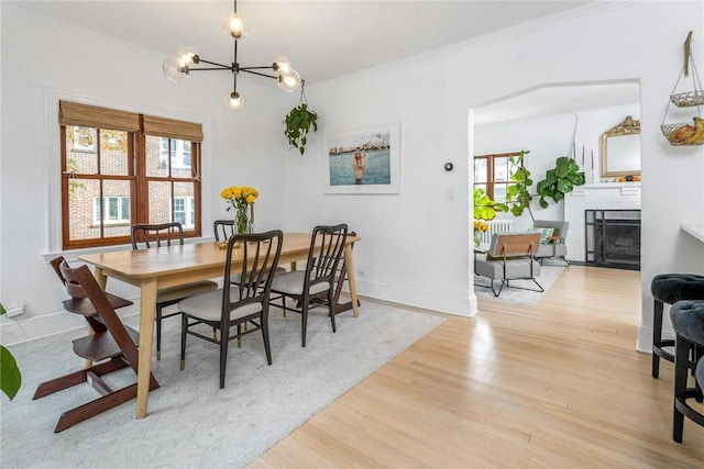 dining room featuring a notable chandelier, baseboards, ornamental molding, a brick fireplace, and light wood-type flooring