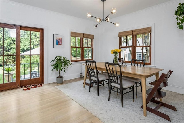 dining area with light wood-style floors, ornamental molding, a wealth of natural light, and an inviting chandelier