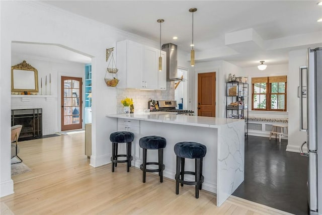 kitchen featuring tasteful backsplash, appliances with stainless steel finishes, a breakfast bar, wall chimney range hood, and white cabinetry