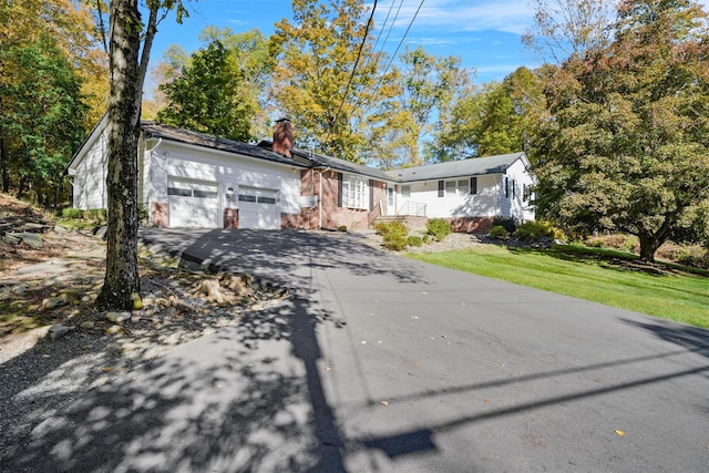 ranch-style house with driveway, an attached garage, a front yard, brick siding, and a chimney