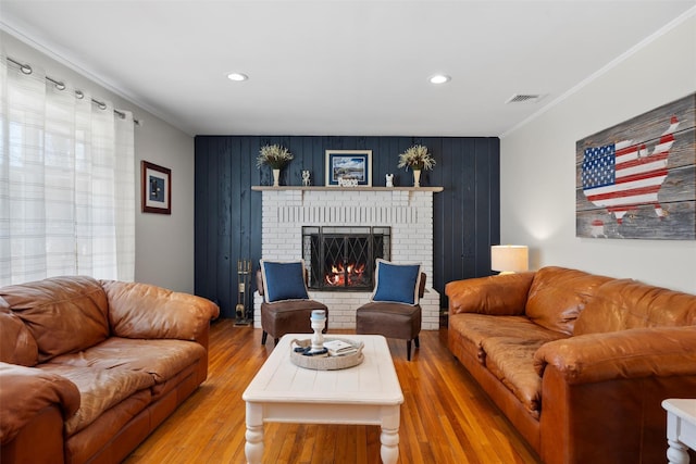 living area with crown molding, a fireplace, visible vents, and light wood finished floors