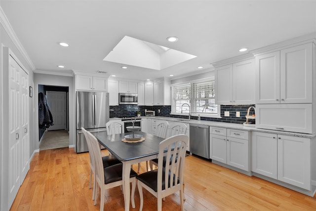 kitchen featuring crown molding, a skylight, white cabinets, stainless steel appliances, and a sink