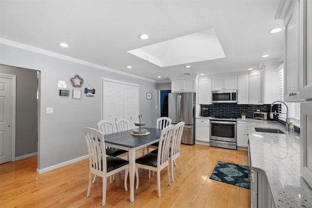 dining area with light wood-style flooring, baseboards, a skylight, and crown molding