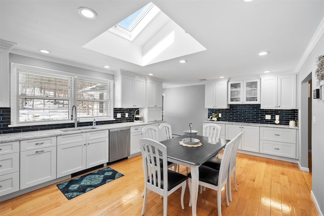 kitchen with light wood-type flooring, a sink, white cabinets, crown molding, and dishwasher