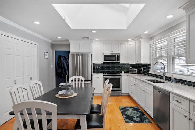 kitchen with light wood-type flooring, ornamental molding, decorative backsplash, appliances with stainless steel finishes, and a sink