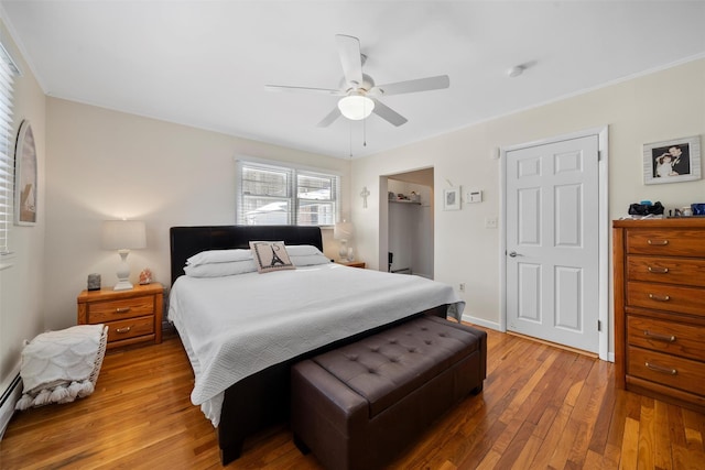 bedroom featuring a walk in closet, baseboards, light wood-style floors, a ceiling fan, and a baseboard radiator