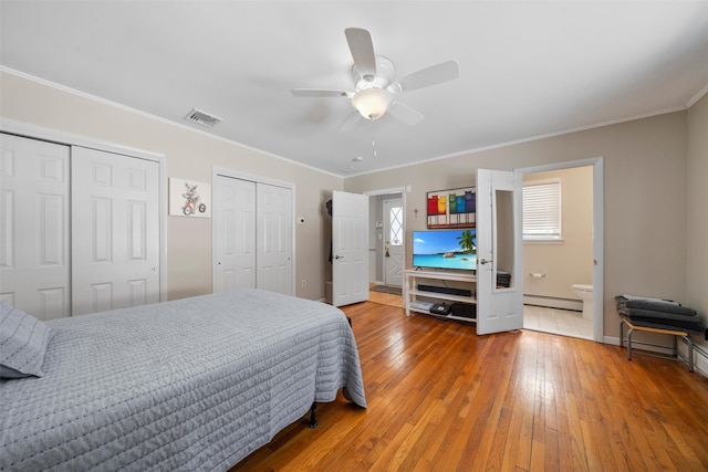 bedroom featuring visible vents, multiple closets, hardwood / wood-style floors, crown molding, and baseboard heating