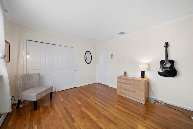 sitting room with hardwood / wood-style floors, visible vents, baseboards, and ornamental molding