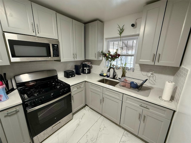 kitchen with a sink, marble finish floor, light countertops, stainless steel microwave, and gas range