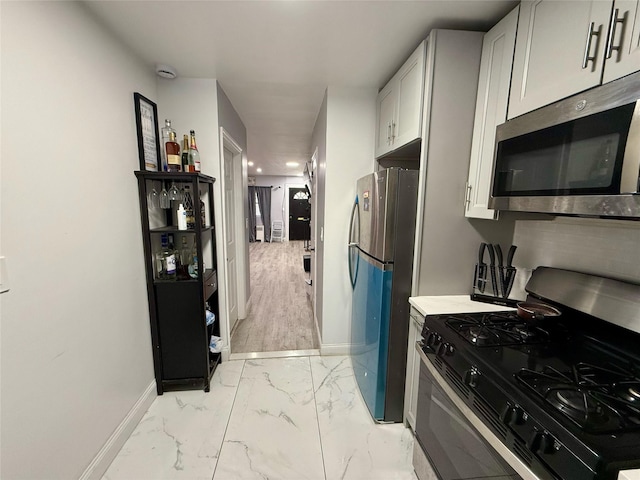 kitchen with baseboards, white cabinets, marble finish floor, light countertops, and appliances with stainless steel finishes