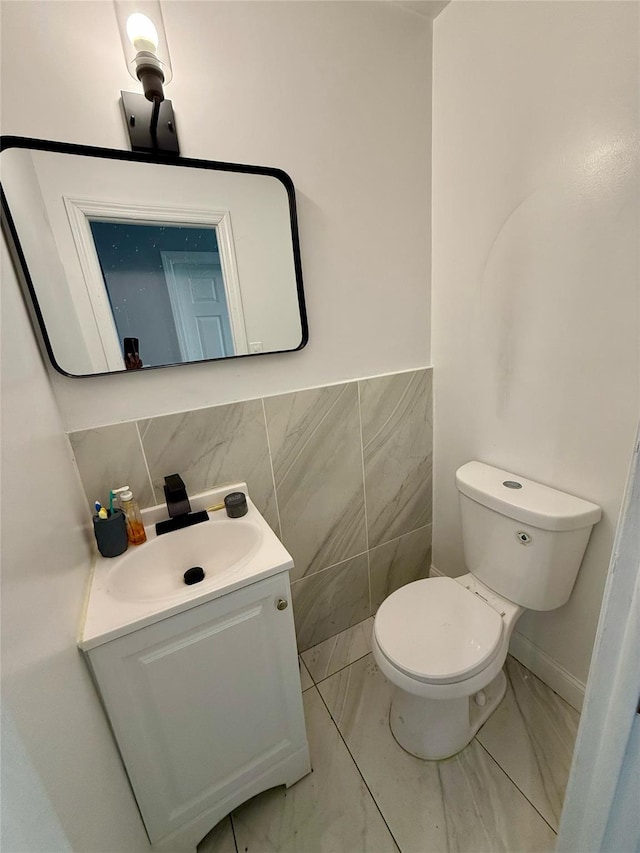 half bathroom featuring toilet, marble finish floor, vanity, and tile walls