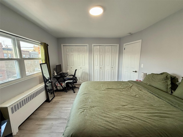 bedroom with light wood finished floors, radiator heating unit, and multiple closets