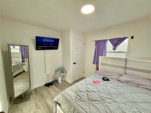 bedroom with radiator heating unit, wood finished floors, and baseboards