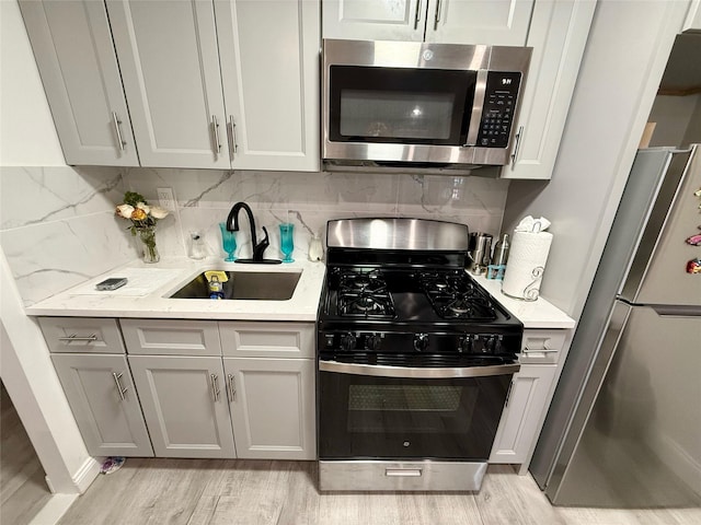 kitchen with light stone counters, stainless steel appliances, a sink, light wood finished floors, and tasteful backsplash