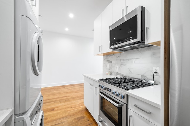 kitchen with light wood finished floors, stainless steel appliances, backsplash, white cabinetry, and stacked washing maching and dryer