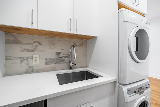 laundry area with stacked washer / drying machine, cabinet space, a sink, and light wood-style flooring