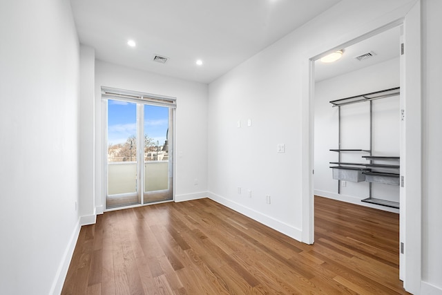 empty room with wood finished floors, visible vents, and baseboards