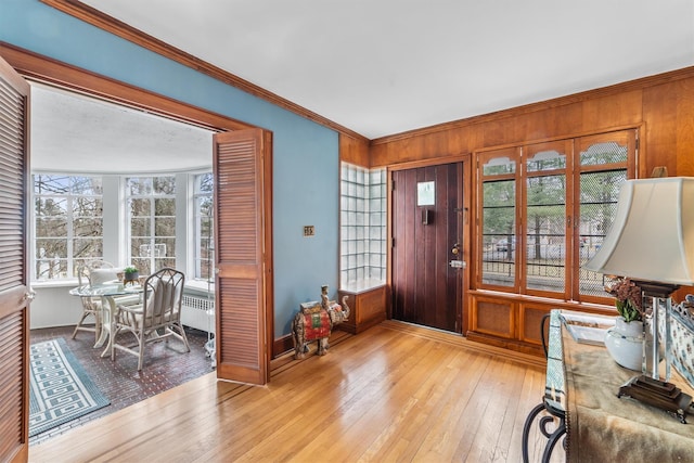 entryway with radiator, light wood-style floors, baseboards, and ornamental molding