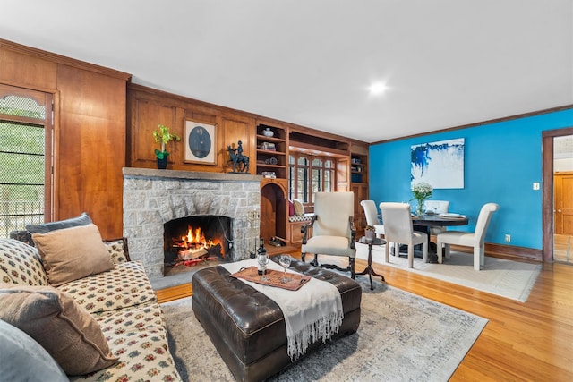 living room featuring built in features, wood finished floors, a stone fireplace, crown molding, and baseboards