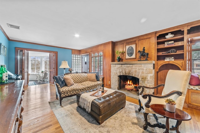 living room featuring light wood finished floors, visible vents, wood walls, ornamental molding, and a stone fireplace