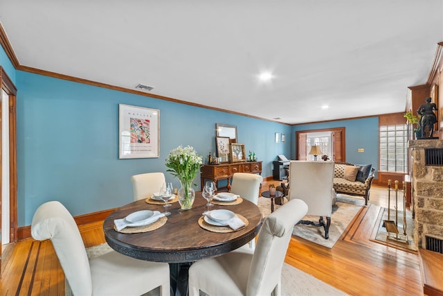 dining space with a stone fireplace, light wood-style flooring, visible vents, and ornamental molding