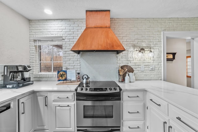 kitchen with custom range hood, light stone counters, white cabinetry, appliances with stainless steel finishes, and decorative backsplash