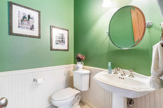 half bathroom featuring toilet, a wainscoted wall, and a sink