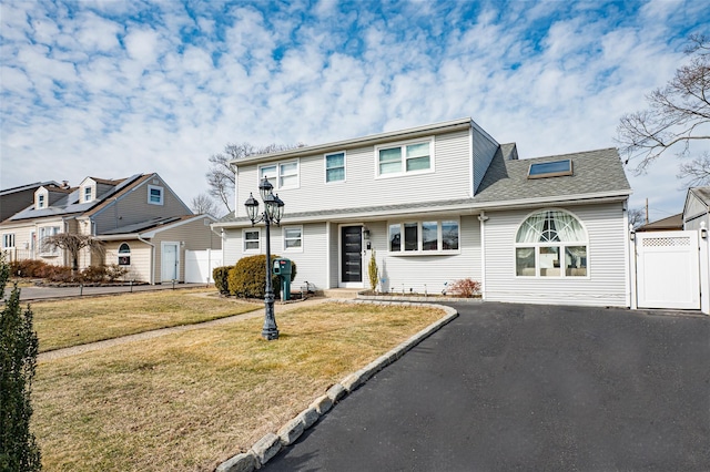 traditional-style home featuring aphalt driveway, a front yard, roof with shingles, and a residential view