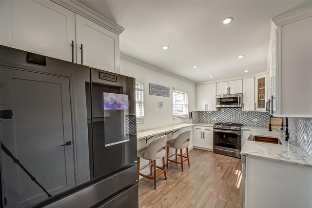 kitchen with light stone counters, appliances with stainless steel finishes, glass insert cabinets, white cabinetry, and a sink